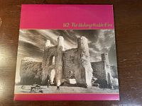 Front cover of U2 vinyl album The Unforgettable Fire with black and white castle image on pink background.