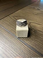 Ring positioned on a small display stand, clear view of the Celtic knot pattern and silver tone.
