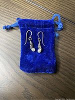 Pair of vintage sterling silver dangle earrings with small white pearl drops displayed on a blue velvet pouch.