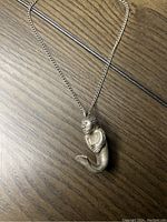 Full view of mermaid pendant and chain laid flat on wooden surface.
