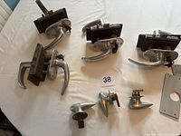 Five airplane door handles with locking mechanisms and keys, two smaller handle parts, a round knob, and a rectangular plate displayed on a white surface.