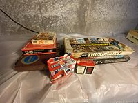 Photo shows stack of board games including Monopoly 60th Anniversary, Torpedo Run, Scrabble, Thunderball, Maverick card game, and Uno card game, as well as small boxes likely containing cards or game pieces.