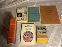 Photo of seven books related to minerals, rocks, mining, including A Book of Precious Stones, Dana's Minerals and How to Study Them, Mining Explained 1, and others.