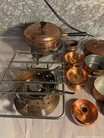 Copper cookware set including chafing dish, burner, candle holders, various pots and pans arranged on a table.