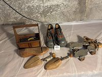 View of platform shoes, shoe shine kit box with brushes, shoetrees, and clip-on skates on table