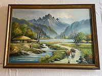 Full view of the framed landscape painting showing rural mountainous scene with huts, trees, and water.