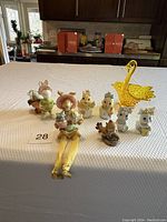 Wide view of all knickknacks arranged on table with kitchen background, showing full lot including yellow glass swan, fabric doll, and ceramic bunnies and chicks.