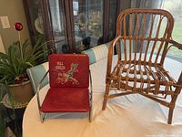 Photo shows vintage red Tom Thumb metal children's chair with cowboy decoration and vintage wicker children's chair side by side on a table.