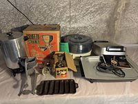 Full lot showing all items: strainer in box, two metal strainers, dehydrator with stacked trays, coffee maker with cord, warming pan, and cast iron corn roaster.