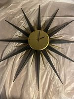 Full view of vintage sunburst wall clock with alternating black and gold metal rays, laid on a white sheet showing overall shape and size.