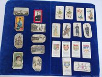 Full lot laid out on a blue velvet background showing 15 chromolitho cards with varied designs including characters, buildings, and heraldry.