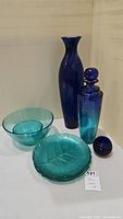 Lot viewed in corner with 6 blue glass pieces: 2 plates, 1 bowl, 2 bottles, and 1 candle holder