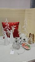 Wide view of the lot showing cushion, four white icicle trees, gold angel, glass house, baubles, and coasters all arranged on table with neutral background.