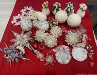Full top view of all ornaments on red cloth showing varied styles, colors mostly white, clear and silver. Includes bird figurines, beaded clusters, snowflakes, balls and icicles.