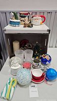 Full view of assorted Christmas-themed items including mugs, candle holders, snow globes, and ornaments
