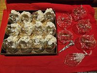 Set of 19 glass Christmas ornaments arranged on a red cloth. Thirteen have white floral fabric tops with crystal-like beads. Six have painted or etched snowflake designs on clear glass.