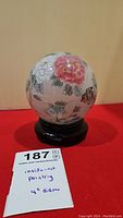 Front view of glass ball with visible pink flower painting inside and black wooden stand.