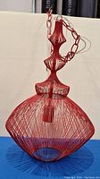 Photo of decorative red metal hanging wire lamp on blue cloth background, front view showing shape and chain.