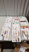 Full view of the assorted lady's sewing patterns spread out on table in neat stacks, brands McCalls, Vogue, Butterick, New Look visible with various garment designs shown on envelopes.