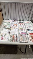 Multiple rows of sewing patterns laid out on a table, mostly for women's clothing, including dresses, jackets, and skirts from McCall's, Simplicity, Butterfly, and New Look.