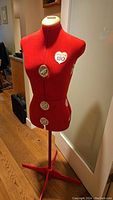 Full front view of the red Singer dress form on tripod stand, showing heart-shaped Singer 150 logo and multiple adjustment dials.