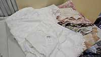 Photo of a pile of folded white, pink, and beige tablecloths showing lace, embroidered, and printed fabric surfaces.