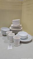 Grouped photo of the dishware set showing stacked bowls, plates and mugs with embossed grapevine design