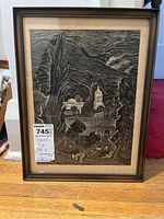 Framed signed art print titled "In a Memory," showing a rural landscape with buildings, trees, and mountains, framed in brown with matting.