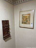 Image showing framed signed mixed media artwork hanging on wall next to wood carving.
