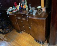Full front angled view showing entire wooden dresser with side compartments, four center drawers, and decorative round metal pulls. Various personal items on top are excluded from sale.
