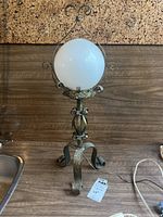 Full view of Art Deco lamp with metal frame and white glass globe on a wooden surface against corkboard background.