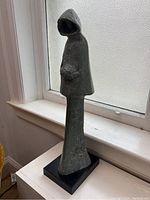 Side view of vintage Austin Productions sculpture depicting winter fashion figure in hooded coat on black base.