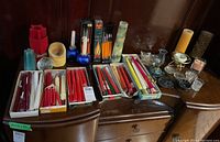 Wide view showing boxes of candles, candle holders, and an oil lamp on wooden furniture