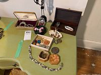 Wide view of assorted costume jewelry pieces displayed on a green table including bracelets, brooches, earrings, jewelry boxes, and figurine ring holder.