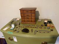Overview of the wooden jewelry chest, glass jewelry box, and assortment of pins, brooches, bracelets, and earrings laid out on a table.