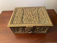 Top and front view of the rectangular brass box showing the intricate embossed cherubs and Rococo floral motifs, and front clasp.