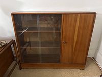 Full front view of the MCM cabinet showing double glass sliding doors on the left and a single wooden compartment door on the right, all resting on a low base.