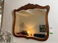 Full view of the vintage beveled mirror mounted on wall, with visible carved wood frame and beveled glass reflecting room interior.