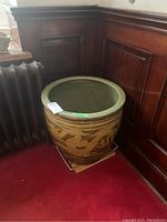 Large round concrete planter with dragon motif, earthy colors, positioned next to wood paneling and radiator on red carpet.