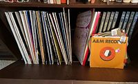 Shelf of vinyl albums and box of 7 inch singles in orange A&M Records sleeves on a wooden shelf.