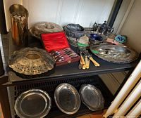 Two shelves filled with a variety of silver plate items including trays, fish cutlery, and other pieces.