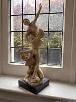 Full view of composite statue with three figures in dynamic composition, standing on dark base with window background.