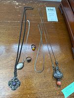 Overview photo showing all jewelry pieces including necklaces, rings, locket, and chains on wooden surface.