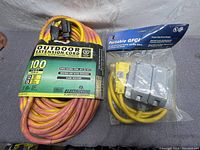 Photo showing coiled 100-foot outdoor extension cord with label describing gauge, length, and safety features next to packaged portable GFCI extension.