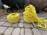 Two yellow spools of heavy duty rope on interlocking stone ground, one spool smaller and compact and the other larger and loosely coiled