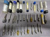 Top-down view of 35 double cut carbide burrs, some in plastic tubes and some loose on fabric surface.