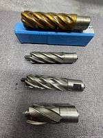 Four annular cutters laid on a grey cloth with one gold coated and three steel cutters to show condition and size.