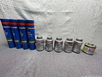 Front view of 4 blue tubes of Chevron heavy-duty grease and 5 silver cans of Loctite anti-seize lubricant and one can of Masters Pro-Dope sealant arranged on gray fabric.