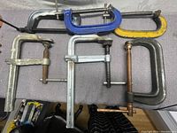 Top down photo showing 6 heavy duty clamps including 4 C clamps and 2 F clamps on a gray surface.