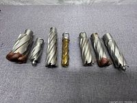 Top and front view of all seven annular cutters showing varying sizes and some rust on one cutter's base.